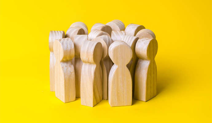 Group of wooden people figurines on a yellow background. Crowd, meeting, social activity. Society, social group. Herd instinct, management of people. Human resources, workers stand together.