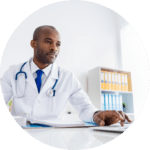 Circular image of doctor sitting at a desk reading data on laptop screen